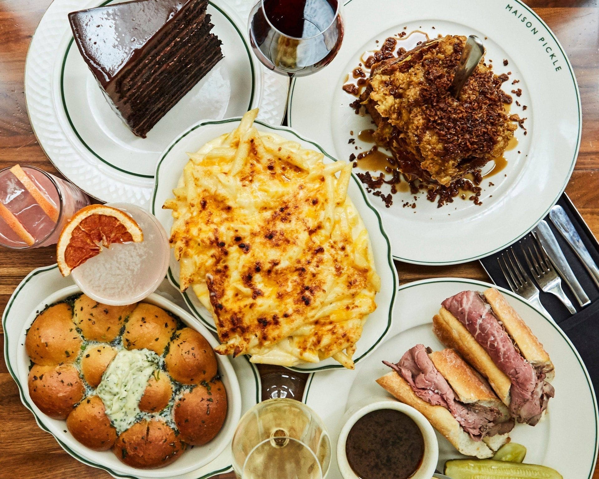 Brunch spread at a popular spot near Central Park, featuring mac and cheese, French dip sandwiches, pull-apart bread with herb butter, crispy fried chicken, and a rich chocolate cake. The meal is accompanied by craft cocktails and wine.