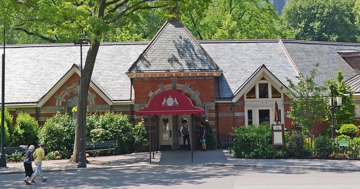 Charming romantic restaurant near Central Park with a historic brick facade, red canopy entrance, and lush greenery, offering an intimate dining experience.