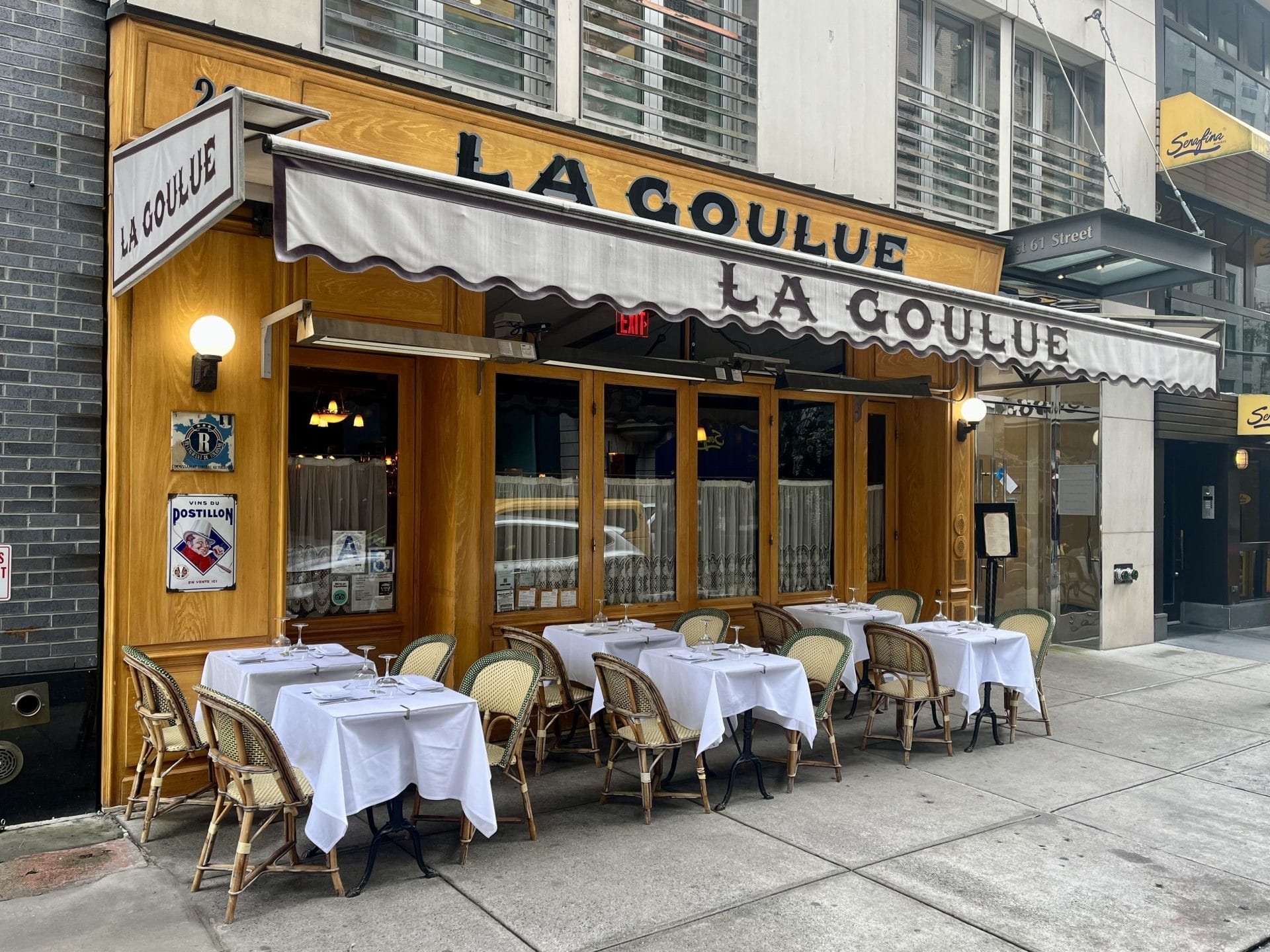 Charming French restaurant near Central Park with classic bistro-style outdoor seating, white tablecloths, and a warm wooden facade, offering an intimate dining atmosphere.