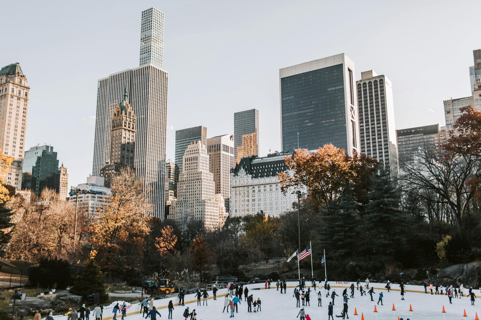 Skyline of New York City with an ice rink at the bottom and people are skating