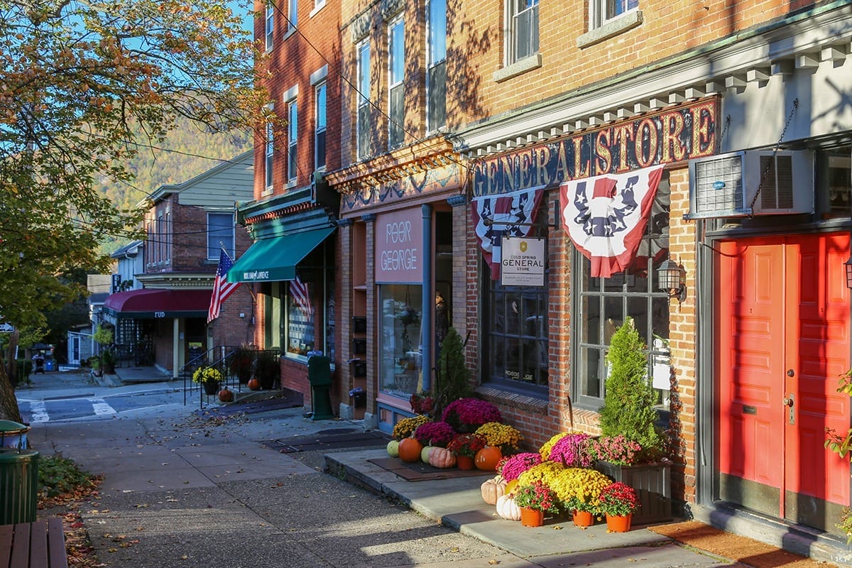 A row of charming shops lining a sidewalk in Cold Spring, New York, showcasing local goods and inviting storefronts. Cool small towns in New York.