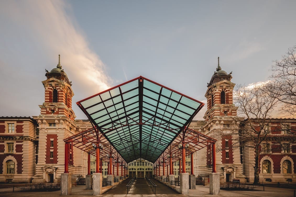 The Ellis Island National Museum of Immigration features a large structure with a glass roof and prominent red pillars.