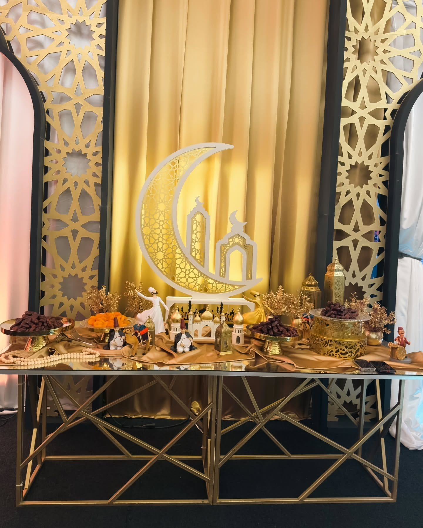 A festive Eid table decorated with gold fabrics, traditional sweets, lanterns, and miniature mosque ornaments, symbolizing Eid gatherings and meals. For the blog post Eid al-Fitr 2025: When Is It And How Do People Celebrate?