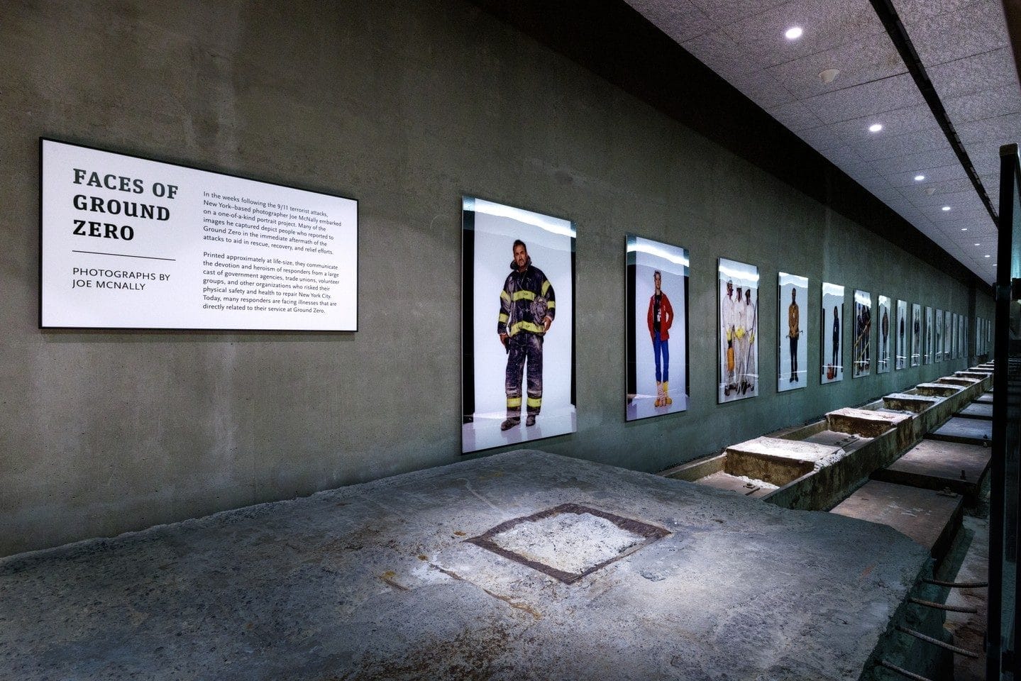 An exhibit at the 9/11 Memorial & Museum titled "Faces of Ground Zero" features a series of large portrait photographs by Joe McNally. The portraits depict first responders, volunteers, and workers involved in the rescue and recovery efforts, displayed along a concrete wall with remnants of the building’s foundation in the foreground. This image is part of the blog post, Zoos, Museums, and Attractions Open on Easter in New York City.