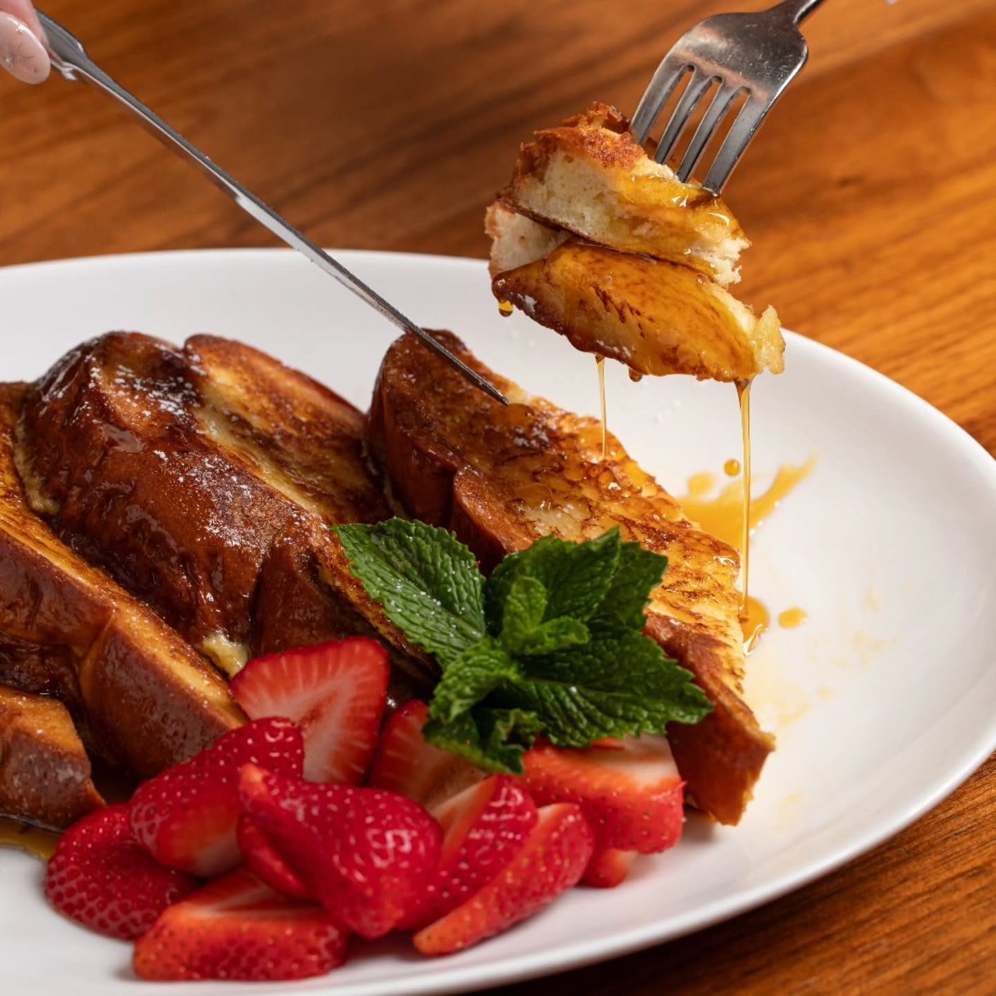 A plate of golden-brown French toast drizzled with syrup, served with fresh strawberries and a sprig of mint at Sarabeth’s. A budget-friendly Easter brunch option that combines classic comfort with a touch of elegance.