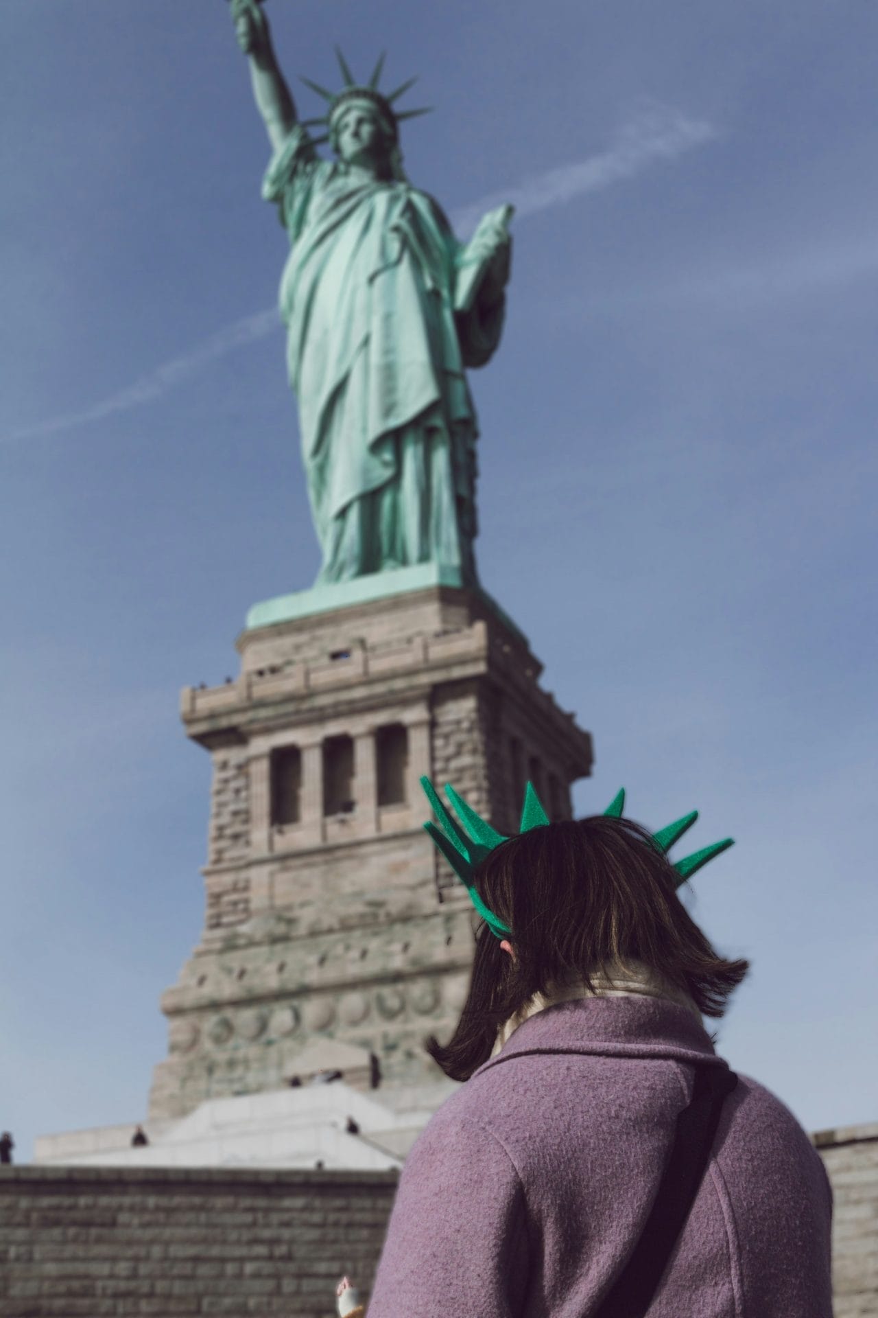 A woman wearing a stylish green hat, facing the statue of liberty in New York