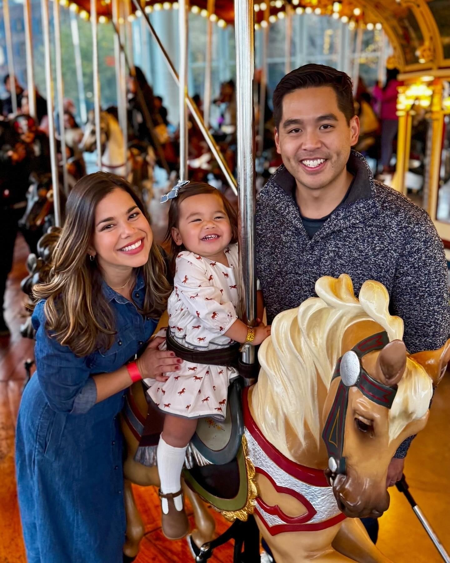 Toddler riding carousel with parents