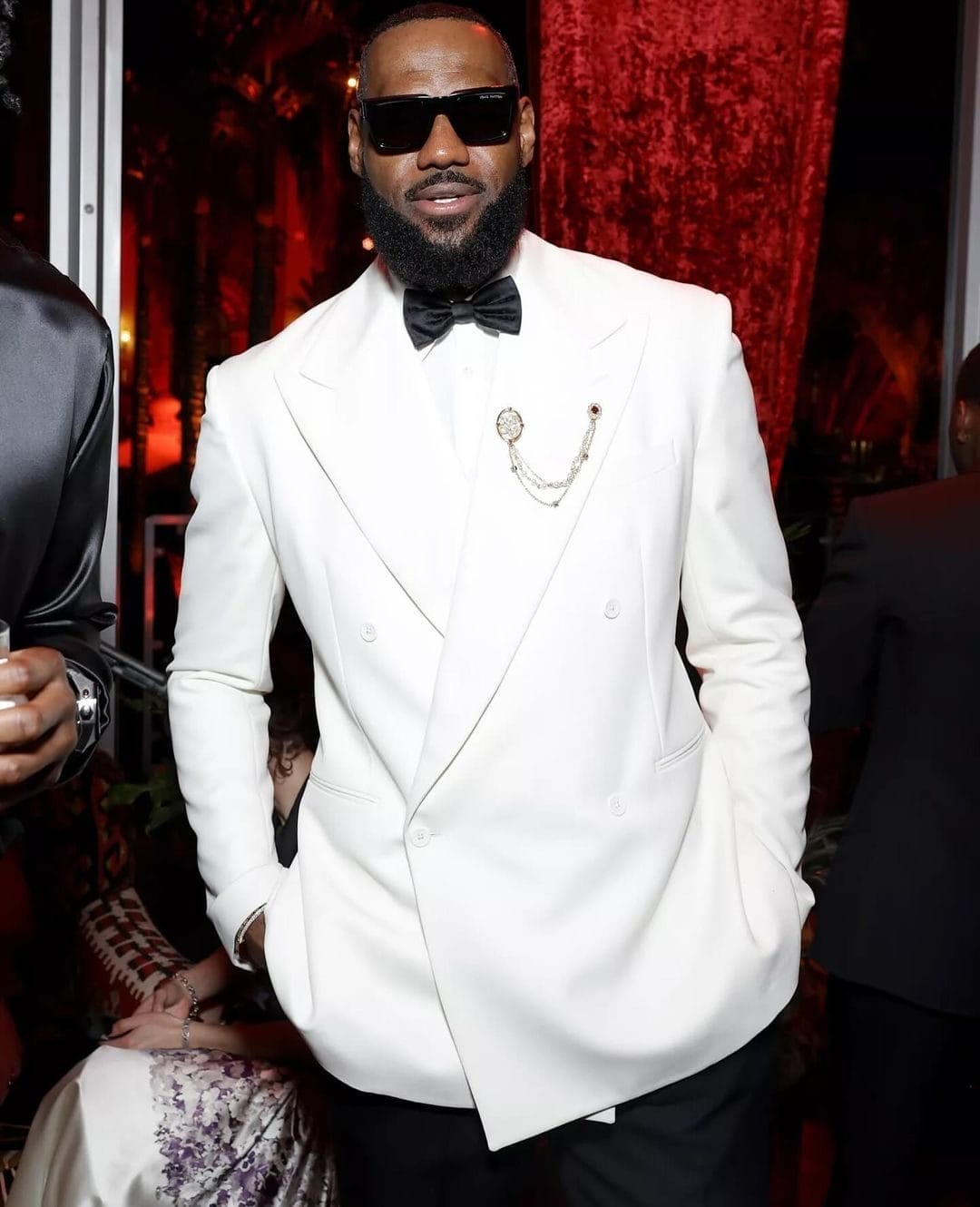 LeBron James wearing a white double-breasted tuxedo jacket with a black bow tie and statement brooch chain.