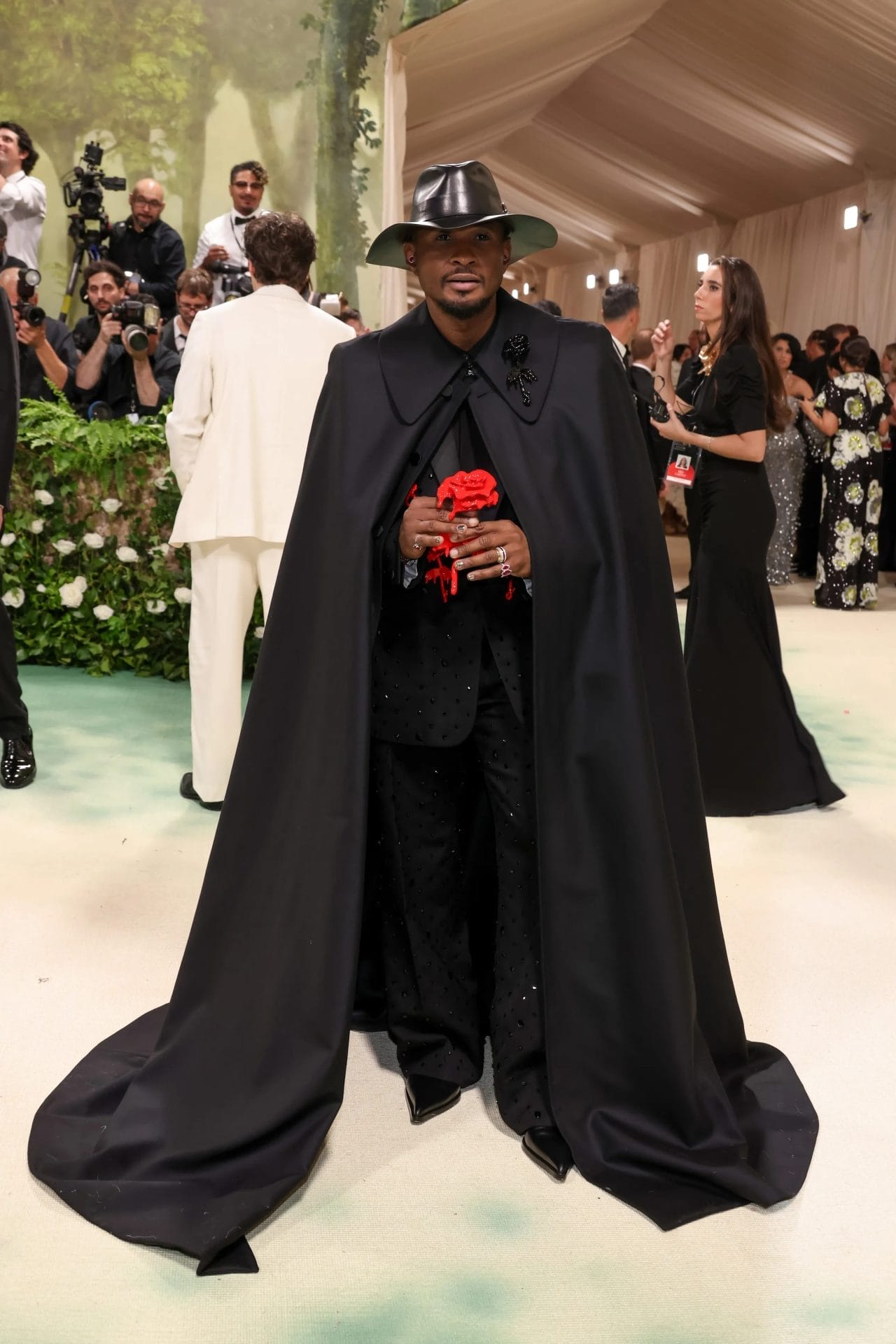 Usher attends the Met Gala wearing a dramatic black cape, studded black suit, and wide-brimmed hat, holding a red wax-dripping rose. Image from Vogue.com for the blog post "Met Gala 2025: Celebrities, Red Carpet, Theme & More."